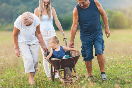 Family pushing their small child and grandchild in a wheelbarrowの写真素材