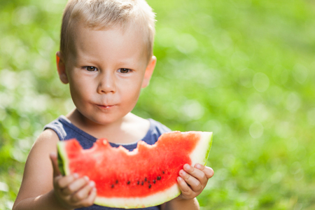 Cute toddler sitting outdoords and eating a slice of watermelonの写真素材