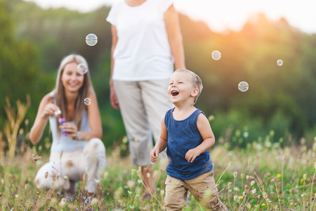 Happy child with family having a great time blowing bubbles outdoorsの写真素材