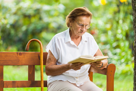 Elderly woman sitting and relaxing on a bench outdoors in parkの写真素材