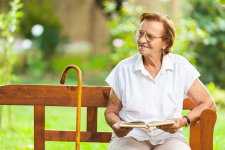 Elderly woman sitting and relaxing on a bench outdoors in parkの写真素材