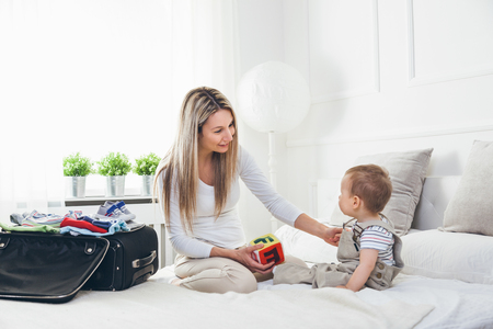 Travelling with kids. Happy mother with her child packing clothes for their holidayの写真素材