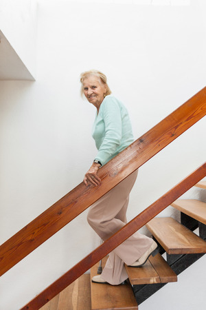 Elderly woman at home using a walking cane to get down the stairsの写真素材