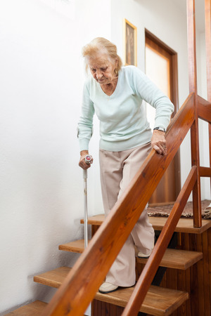 Elderly woman at home using a walking cane to get down the stairsの写真素材