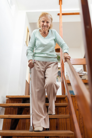 Elderly woman at home using a walking cane to get down the stairsの素材 [FY310118972336]