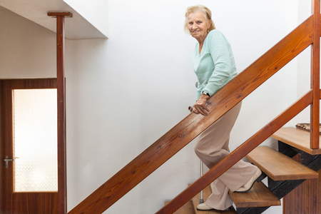 Elderly woman at home using a walking cane to get down the stairsの写真素材