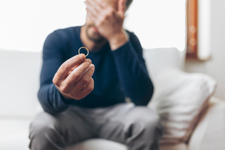 Heartbroken man at home holding a wedding ringの写真素材