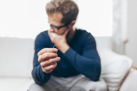 Heartbroken man at home holding a wedding ringの写真素材