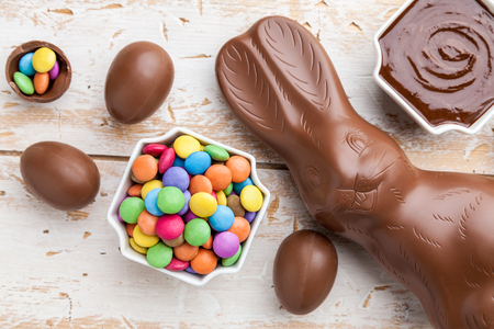 Delicious chocolate Easter bunny, eggs and sweets on rustic background