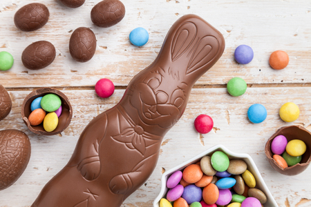 Delicious chocolate Easter bunny, eggs and sweets on rustic background