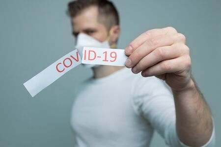 Worried man wearing a respiratory mask, holding the Coronavirus Covid-19 signの写真素材