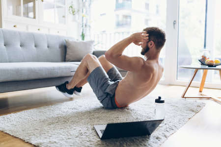 Handsome young man working out at home in the living roomの写真素材