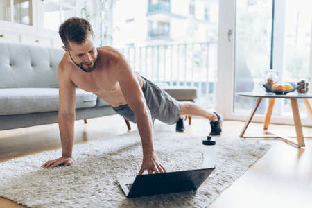 Handsome young man working out at home in the living roomの写真素材