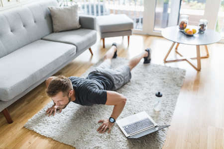 Handsome young man working out at home in the living roomの写真素材
