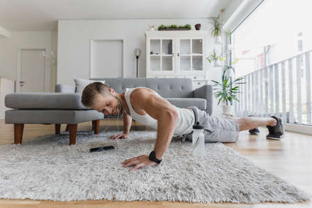 Handsome young man working out at home in the living roomの写真素材