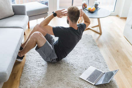 Handsome young man working out at home in the living roomの写真素材