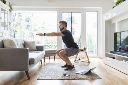 Handsome young man working out at home in the living roomの写真素材