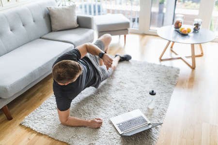 Handsome young man working out at home in the living roomの写真素材
