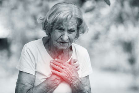 Elderly woman outdoors with heart pain holding her chest