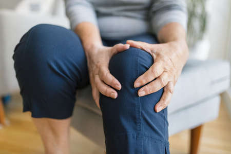 Senior woman sitting on bench, holding her painful kneeの写真素材