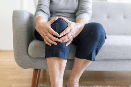 Senior woman sitting on bench, holding her painful kneeの写真素材