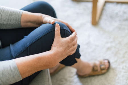 Senior woman sitting on bench, holding her painful kneeの写真素材