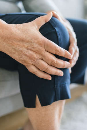 Senior woman sitting on bench, holding her painful kneeの写真素材