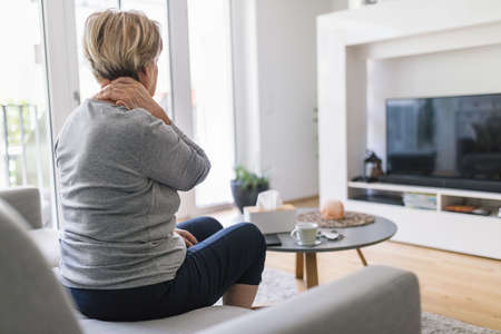 Senior woman in the living room with neck painの写真素材