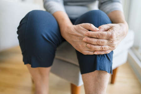 Senior woman sitting on bench, holding her painful kneeの写真素材