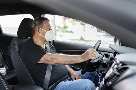 Senior in his 70s driving a car wearing face mask for protection against corona virusの写真素材