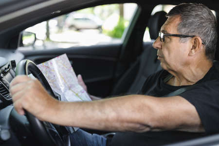 Senior behind the steering wheel of a car, looking at map for directionsの写真素材