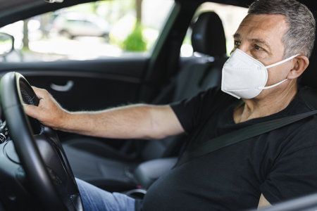 Senior in his 70s driving a car wearing face mask for protection against corona virusの写真素材