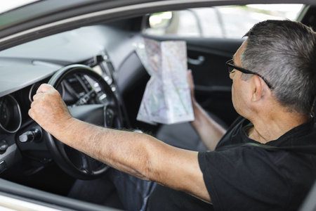 Senior behind the steering wheel of a car, looking at map for directionsの写真素材