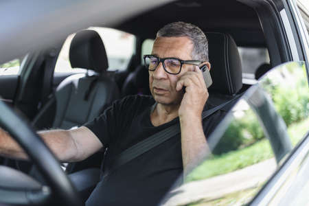Active senior in his 70s driving a car and usig his mobile phoneの写真素材