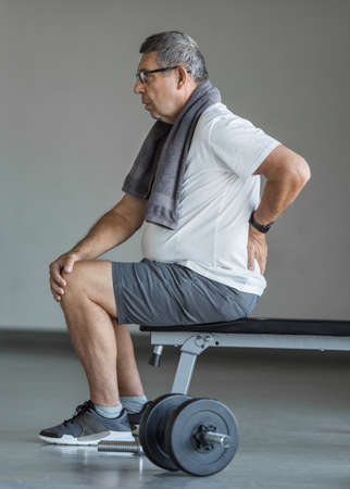 Active senior man in gym with back painの写真素材