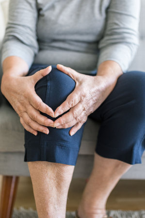 Senior woman sitting on bench, holding her painful kneeの写真素材