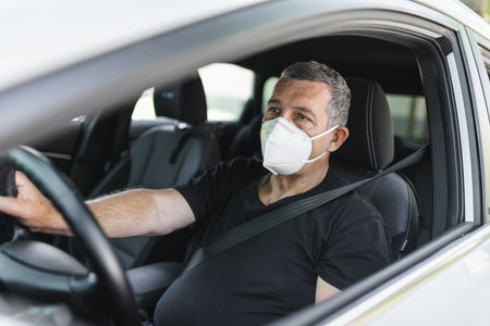 Senior in his 70s driving a car wearing face mask for protection against corona virusの写真素材