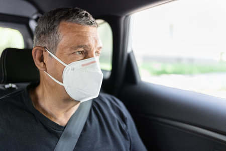 Senior in his 70s sitting at the back of car wearing a face mask for protection against corona virusの写真素材