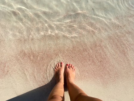 Women's feet on the pink sand (Sicily, Italy)