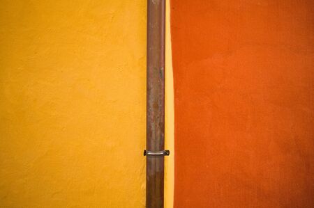 Isolated metallic gutter tube in a red and yellow wall background (Prague, Czech Republic, Europe)