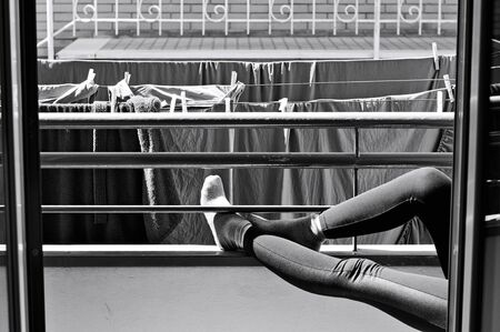 A woman with leggings and socks is relaxing in the balcony near towels hanging on a clotheshorse...