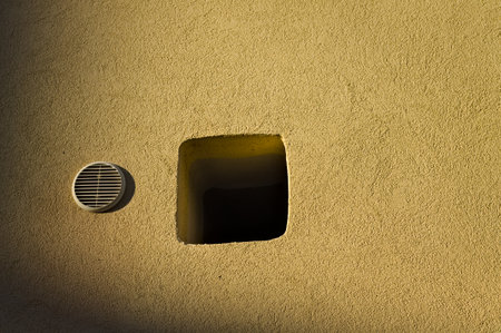 A small hole near the air vent in a yellow wall of a house (Pesaro, Italy, Europe)