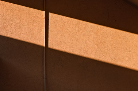A small utility pipe snapped to an orange wall with lights and shadows (Pesaro, Italy, Europe)