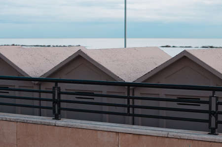 A series of white beach cabins behind a steel fence on the italian coast (Pesaro, Italy, Europe)の写真素材
