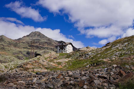 An isolated white house in the italian Alps with mountains and cloudsの写真素材