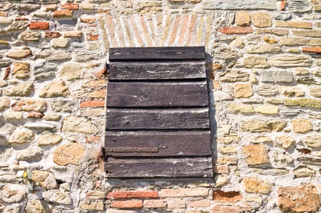 An old wooden shutter that closes a window of a stone house in a medieval Italian villageの写真素材