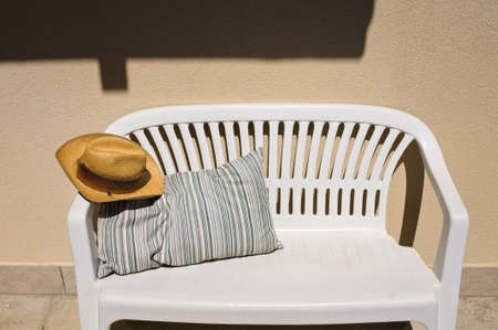 A cowboy wicker hat on a white bench with a striped vintage cushion in the gardenの写真素材