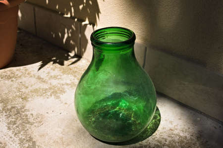 An empty green blown glass vase resting on the ground in the gardenの写真素材