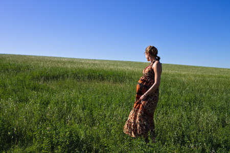 A pregnant blonde girl in a colorful dress is relaxing in a green meadow on a sunny spring day (Marche, Italy, Europe)の写真素材