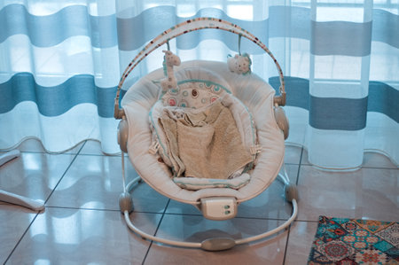 A baby bouncer with toys and towels on the ground in front of a striped curtain in the living room...